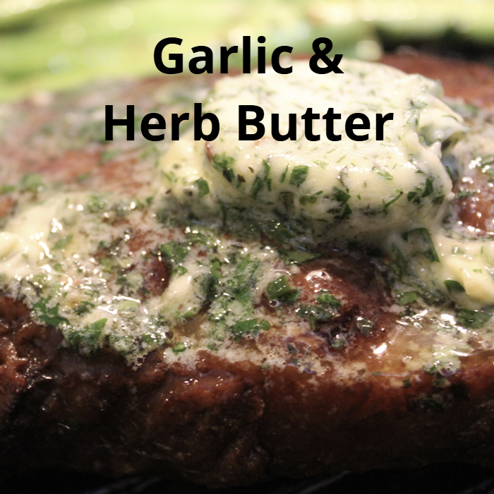 A log of compound butter made with unsalted butter, minced garlic, chives, rosemary, thyme, flat leaf parsley, lemon zest, lemon juice, salt, and a pinch of chili pepper, wrapped in plastic wrap and ready to be chilled.  Delicious over steak, fish or veggie dishes.