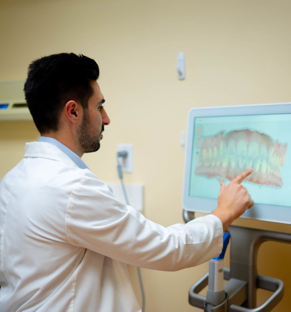 Dr. Mamaliger in a lab coat is pointing at a screen with a picture of teeth on it