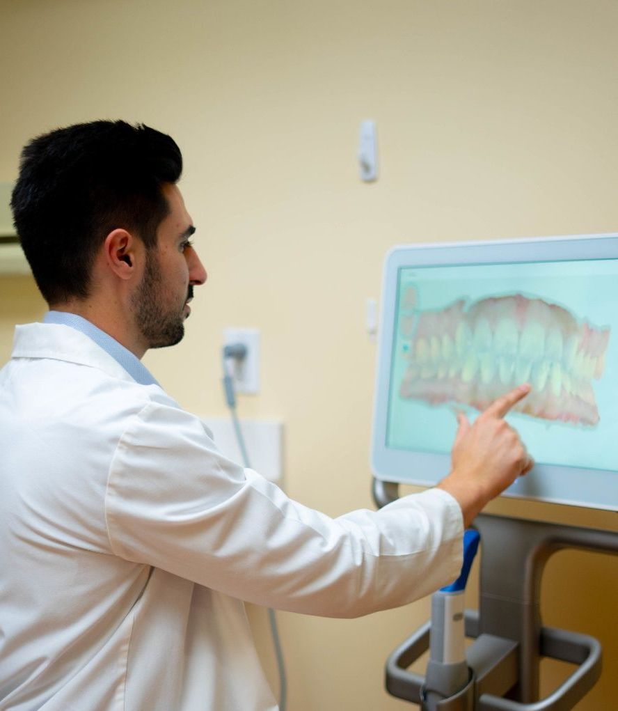 Dr. Mamaliger in a lab coat is pointing at a screen with a picture of teeth on it