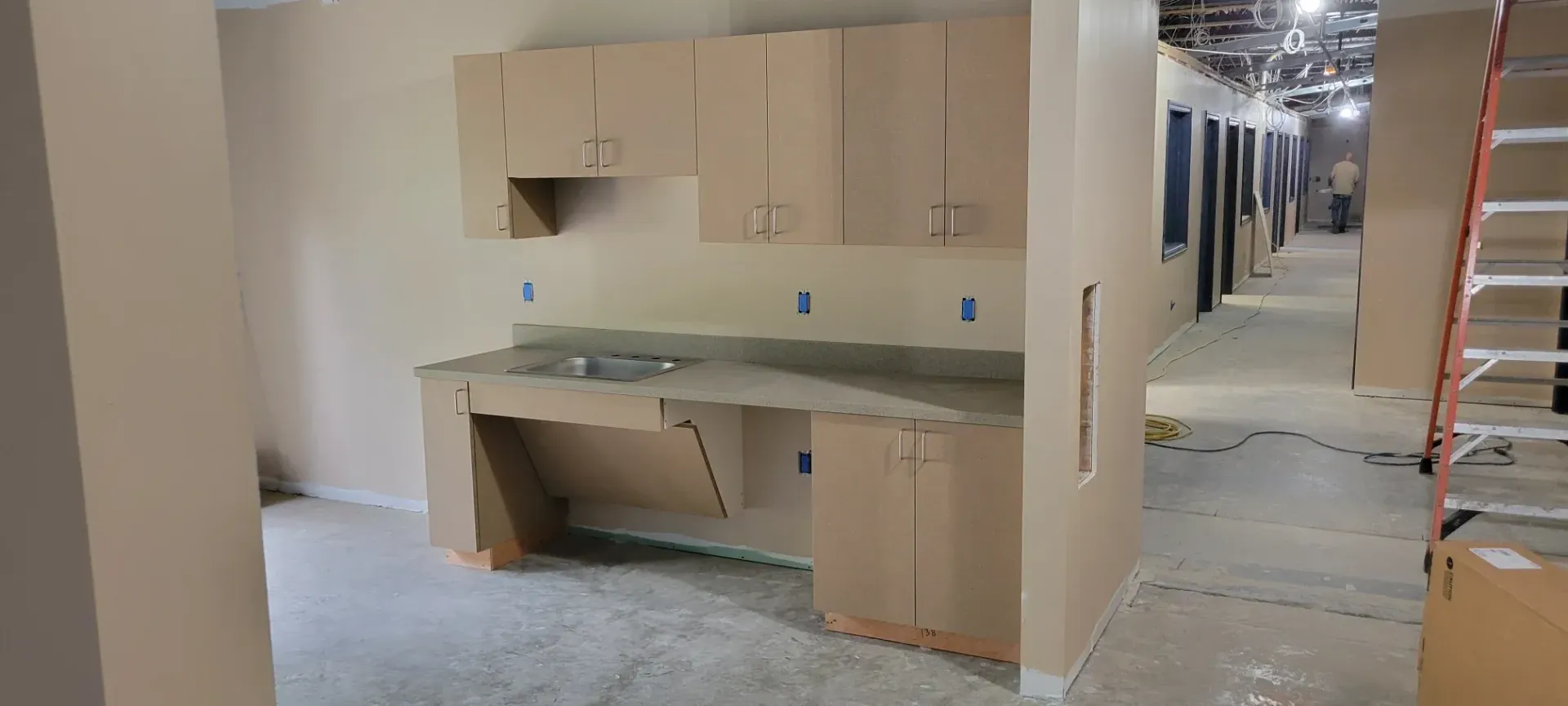 Kitchen cabinets installed in an unfinished room with exposed floors and hallway under construction