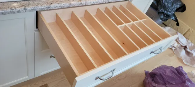 Open drawer with wooden dividers and white sides, likely a kitchen organizer