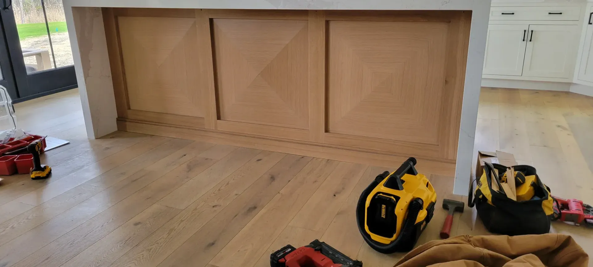 Wood kitchen island with two yellow toy drills on the floor and a red toy truck in the background