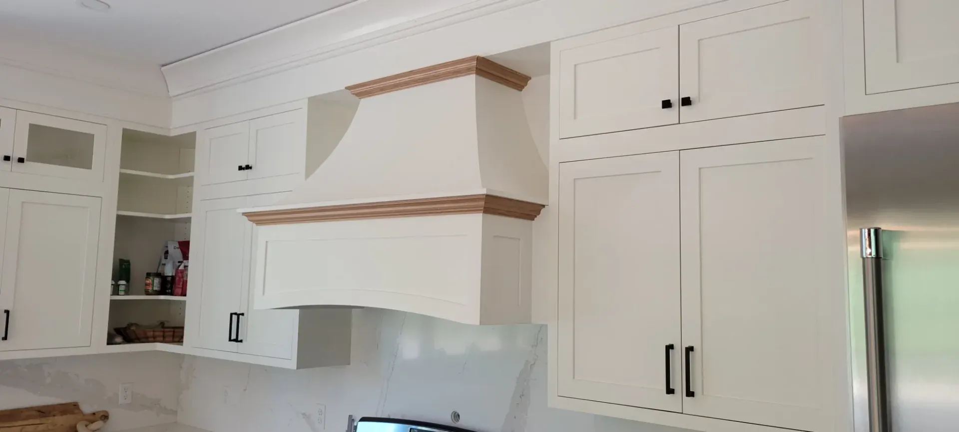 White kitchen cabinets and range hood with wood trim in a bright room