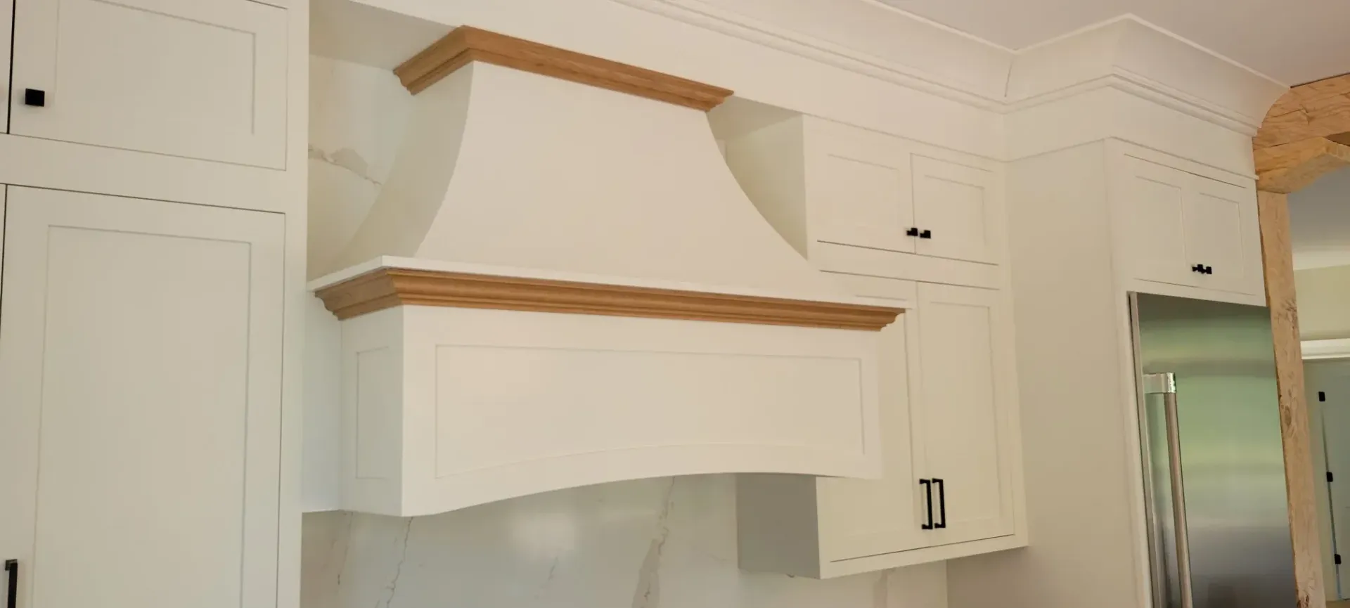White kitchen cabinets with wood trim and a built-in range hood above a stove area