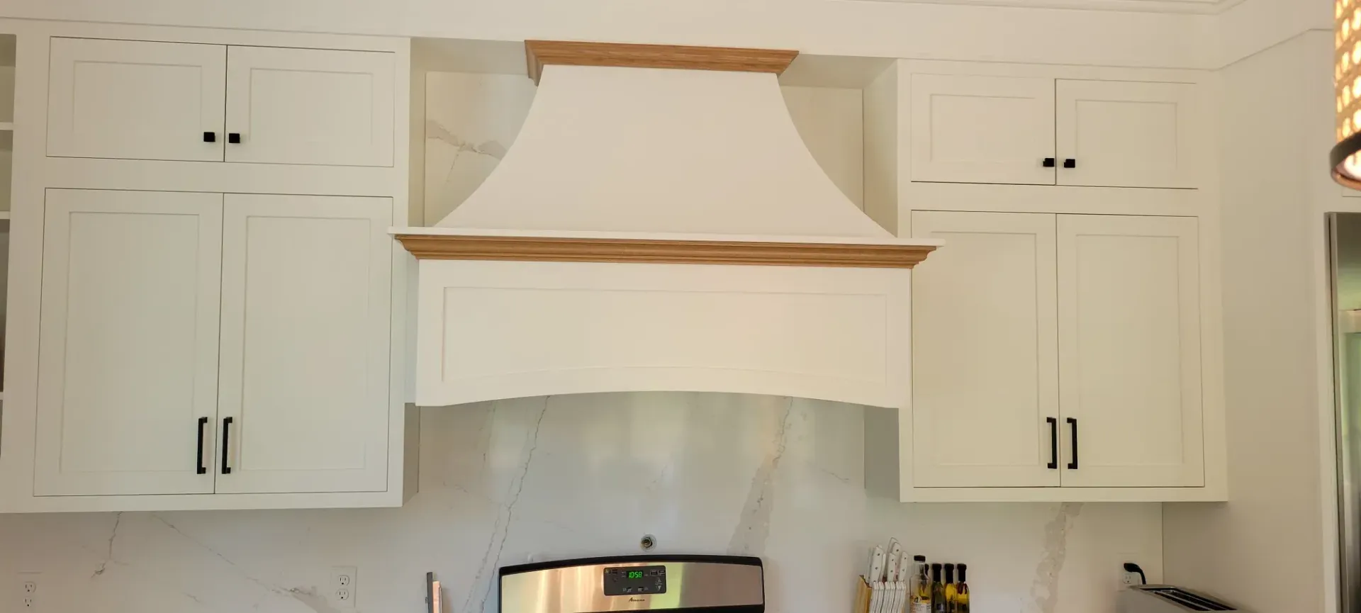 White kitchen cabinets framing a wooden range hood above a stove.