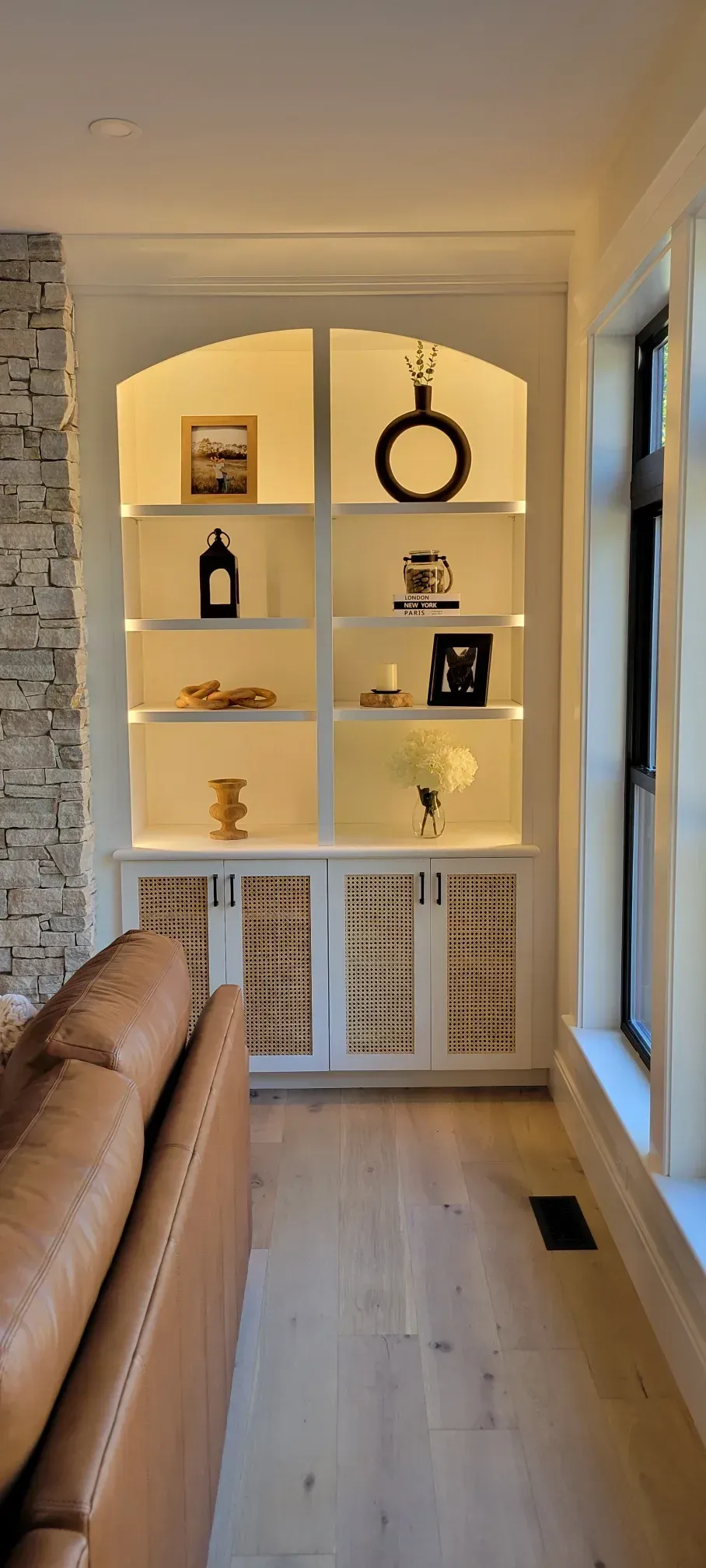 Built-in white shelves with decor in a bright hallway beside a tan sofa and window