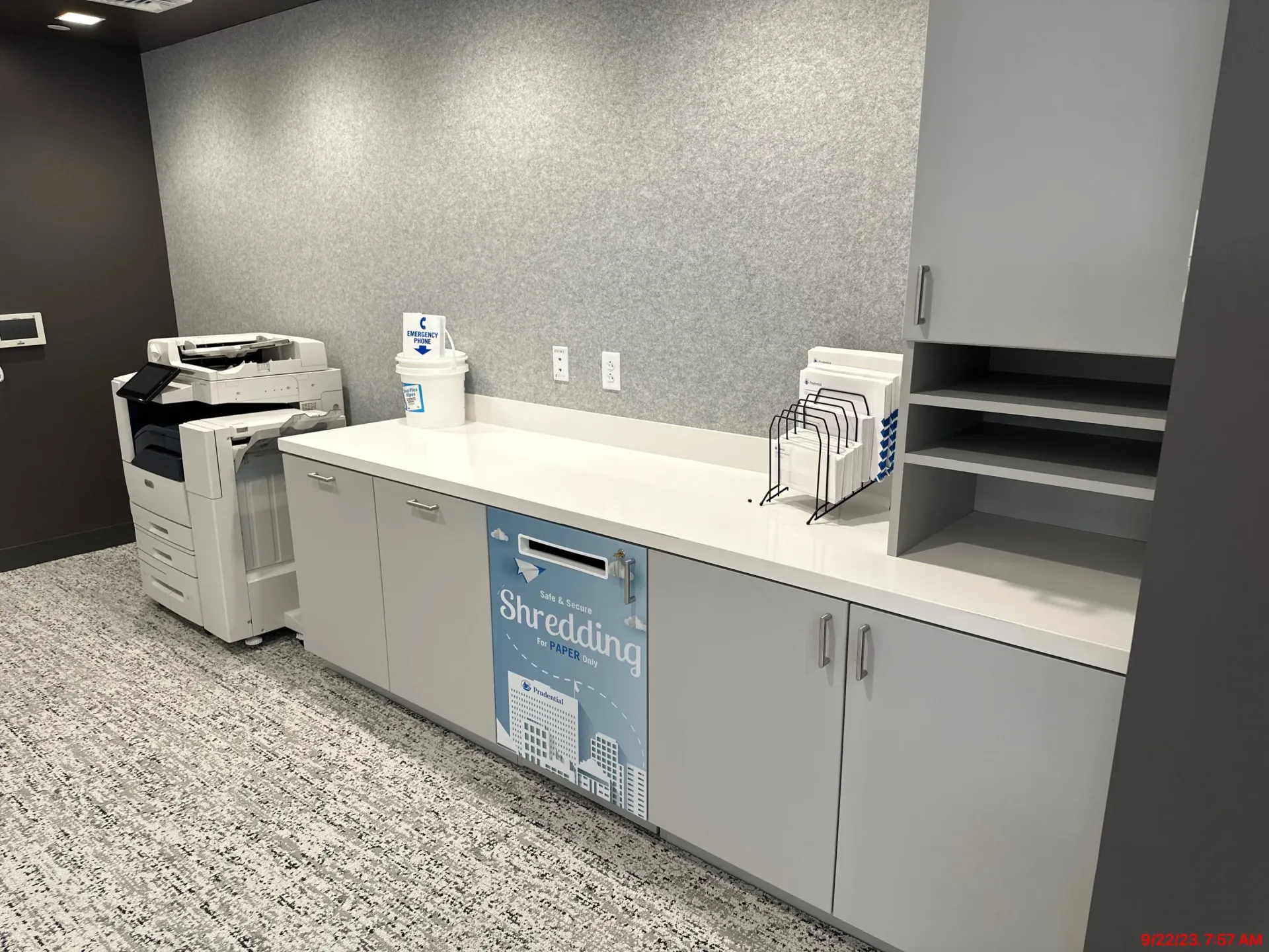Office break room with gray cabinets, countertop appliances, and a copier against a speckled floor.