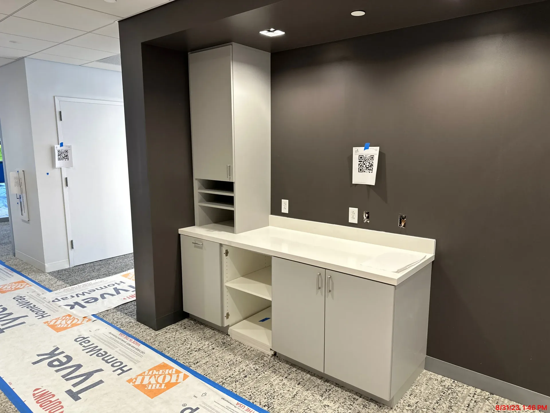 Modern office break room with gray cabinets, white countertop, and dark accent wall.