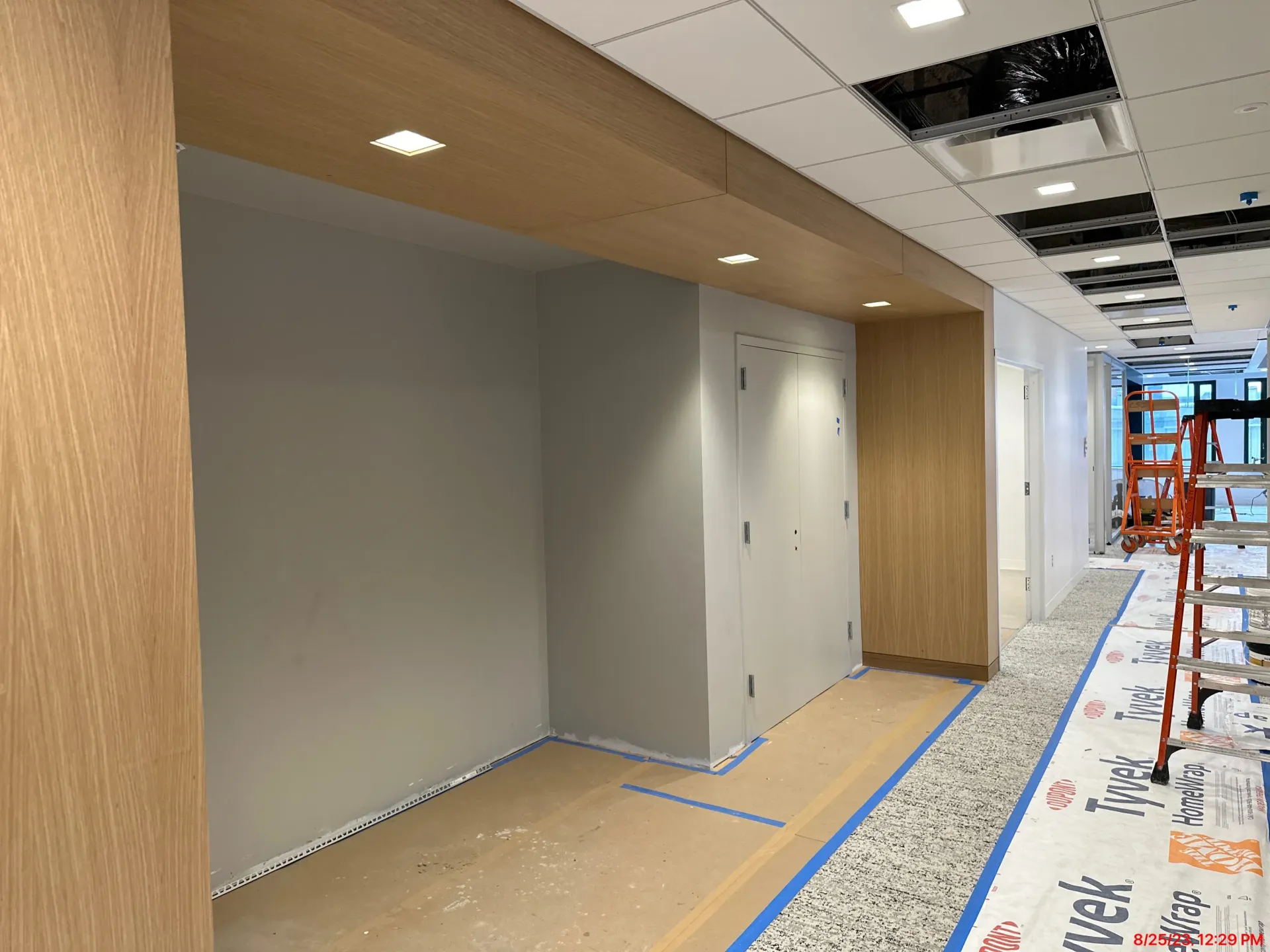 Empty office hallway under renovation with gray walls, wood panels, and protective floor covering