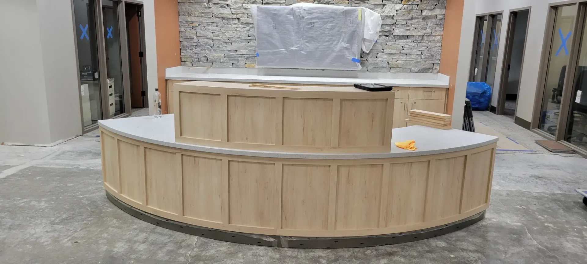 Curved wooden reception counter under construction in a stone-walled interior room