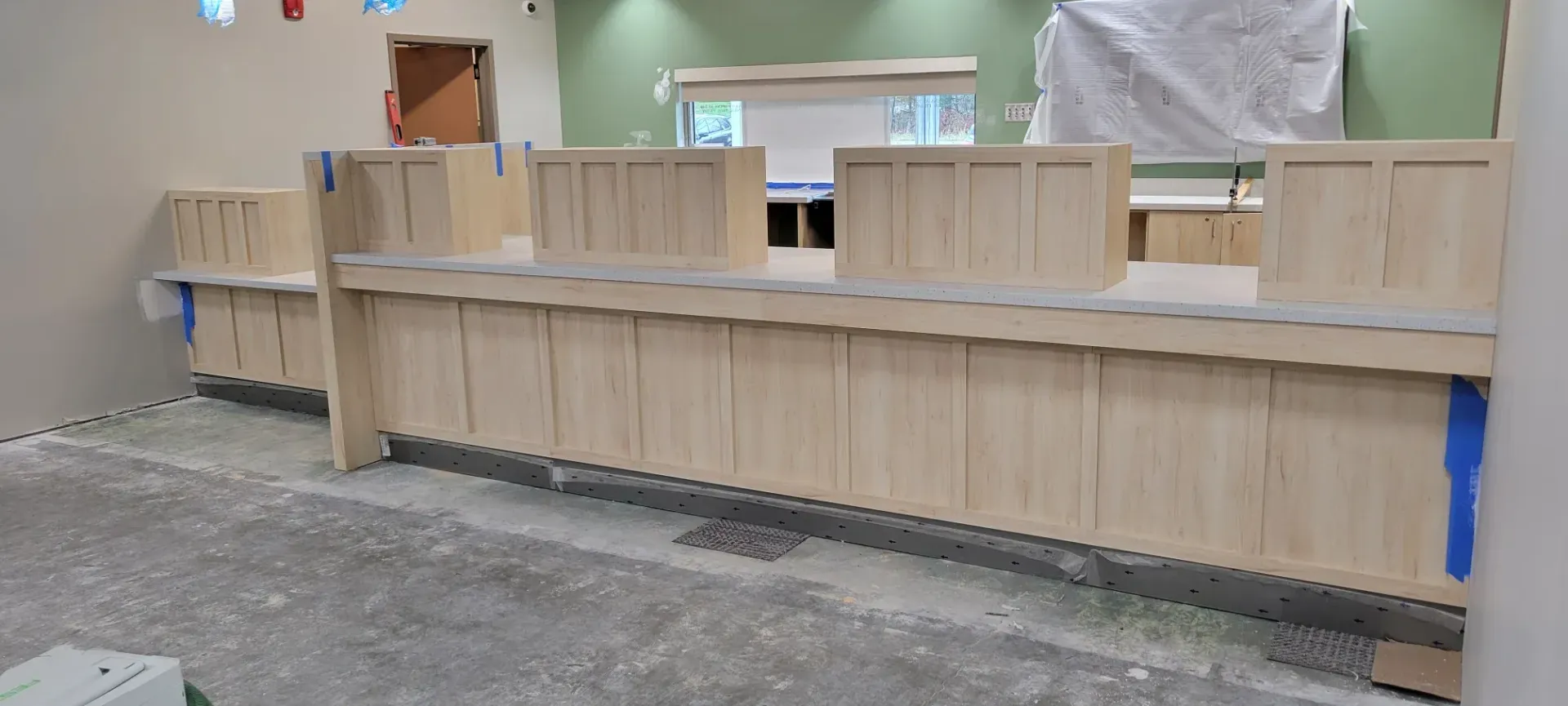 Long beige wooden wall panels under construction in an indoor worksite, with a ladder and tools nearby