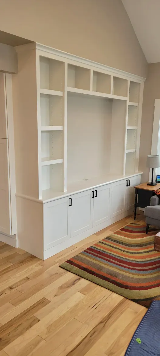 Built-in white wall shelves and cabinets in a bright room with hardwood floors and a striped rug.