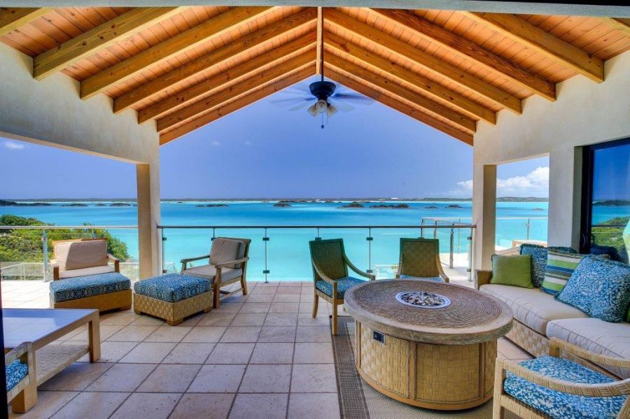 Covered seaside patio with wicker seating, tiled floor, and ocean view under a wooden roof