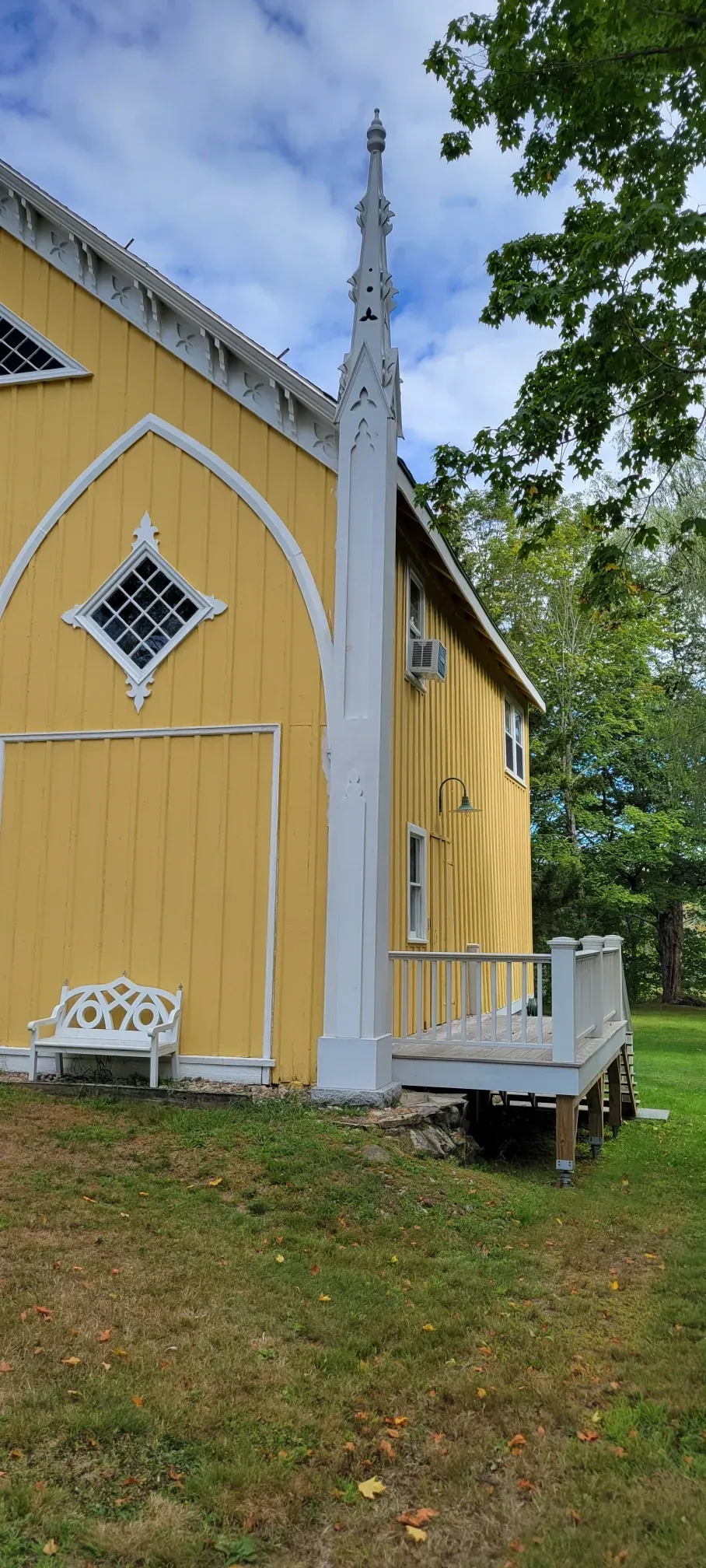 Yellow house with white trim, diamond window, and a small white porch under a cloudy sky