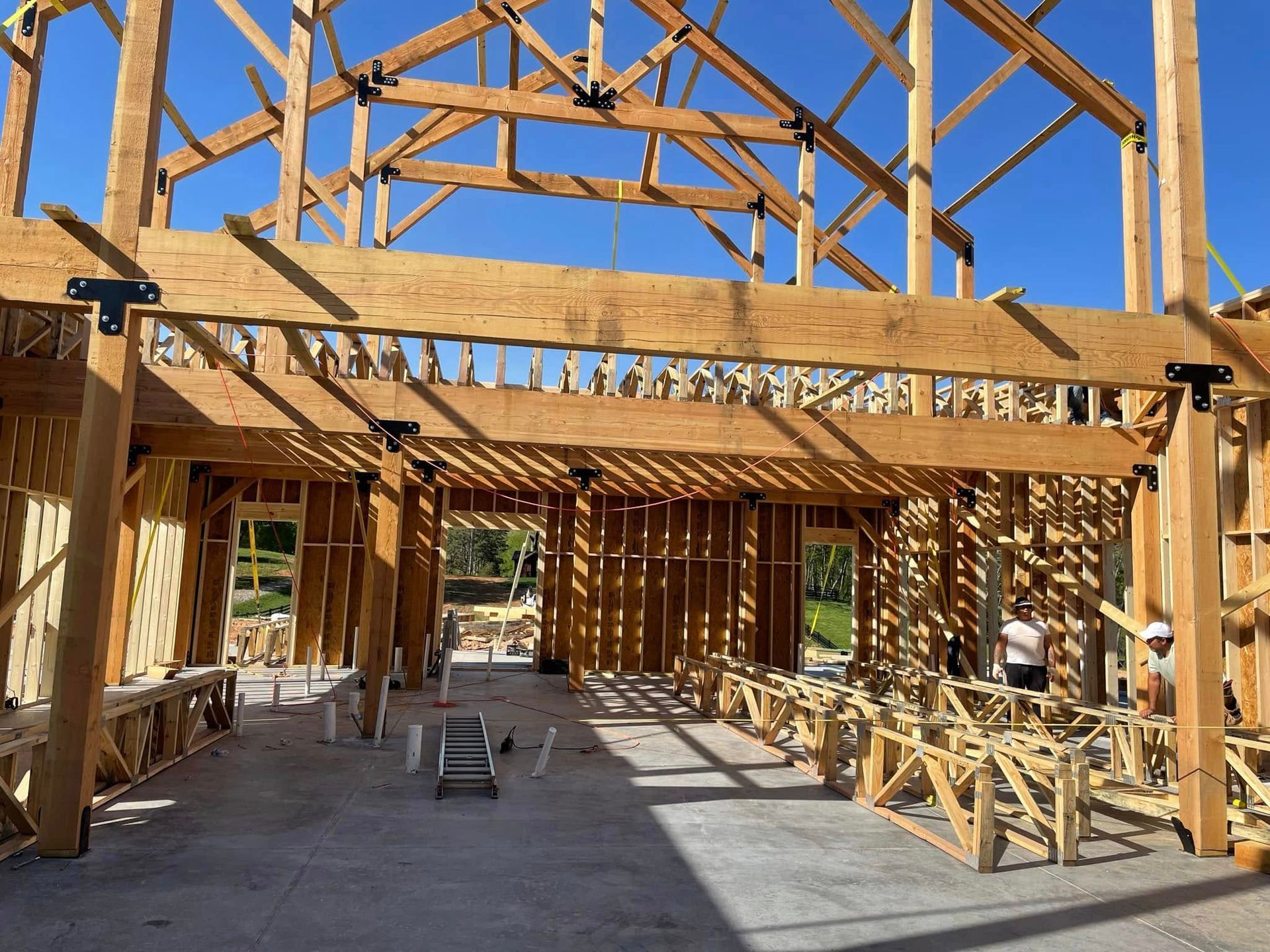 Partially built wooden house framing with exposed beams and roof trusses inside an unfinished construction site