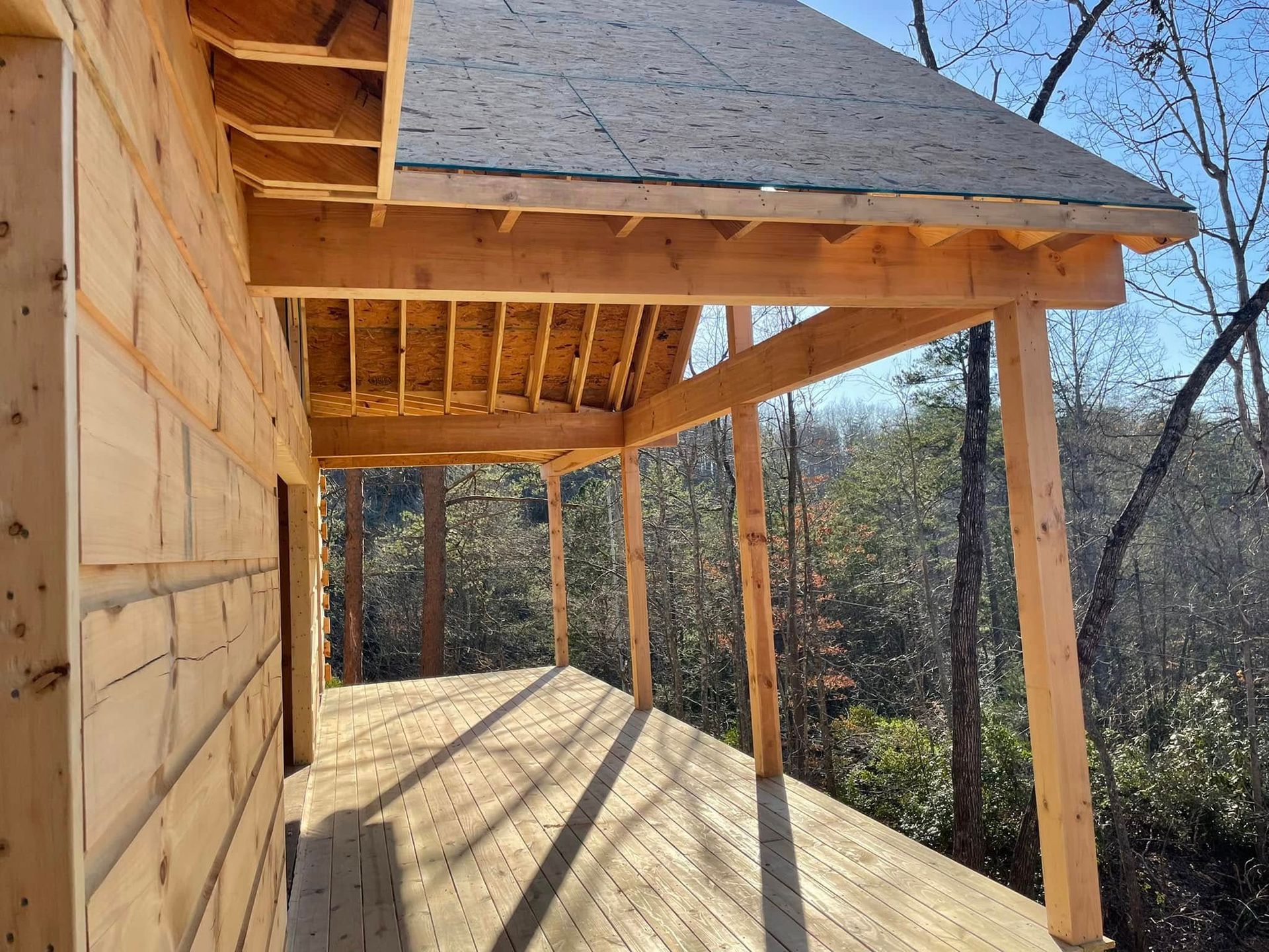 Wooden porch with exposed beams and roof framing overlooking a wooded hillside