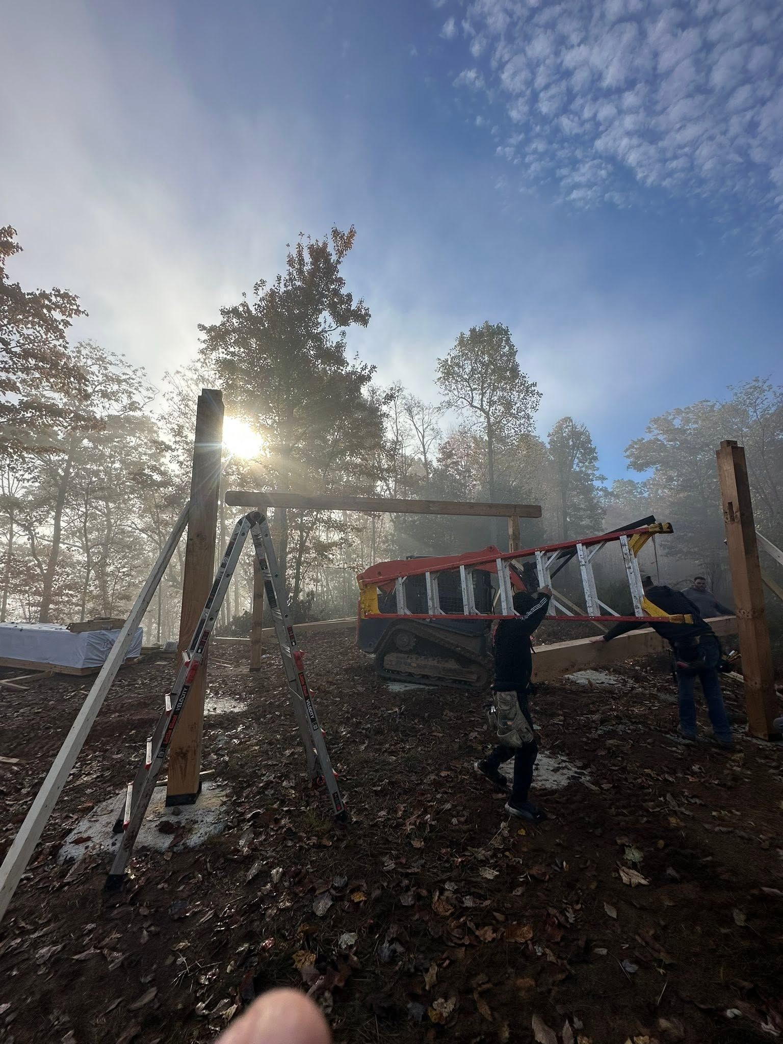 People using a ladder and ropes on a play structure at sunset in a wooded yard