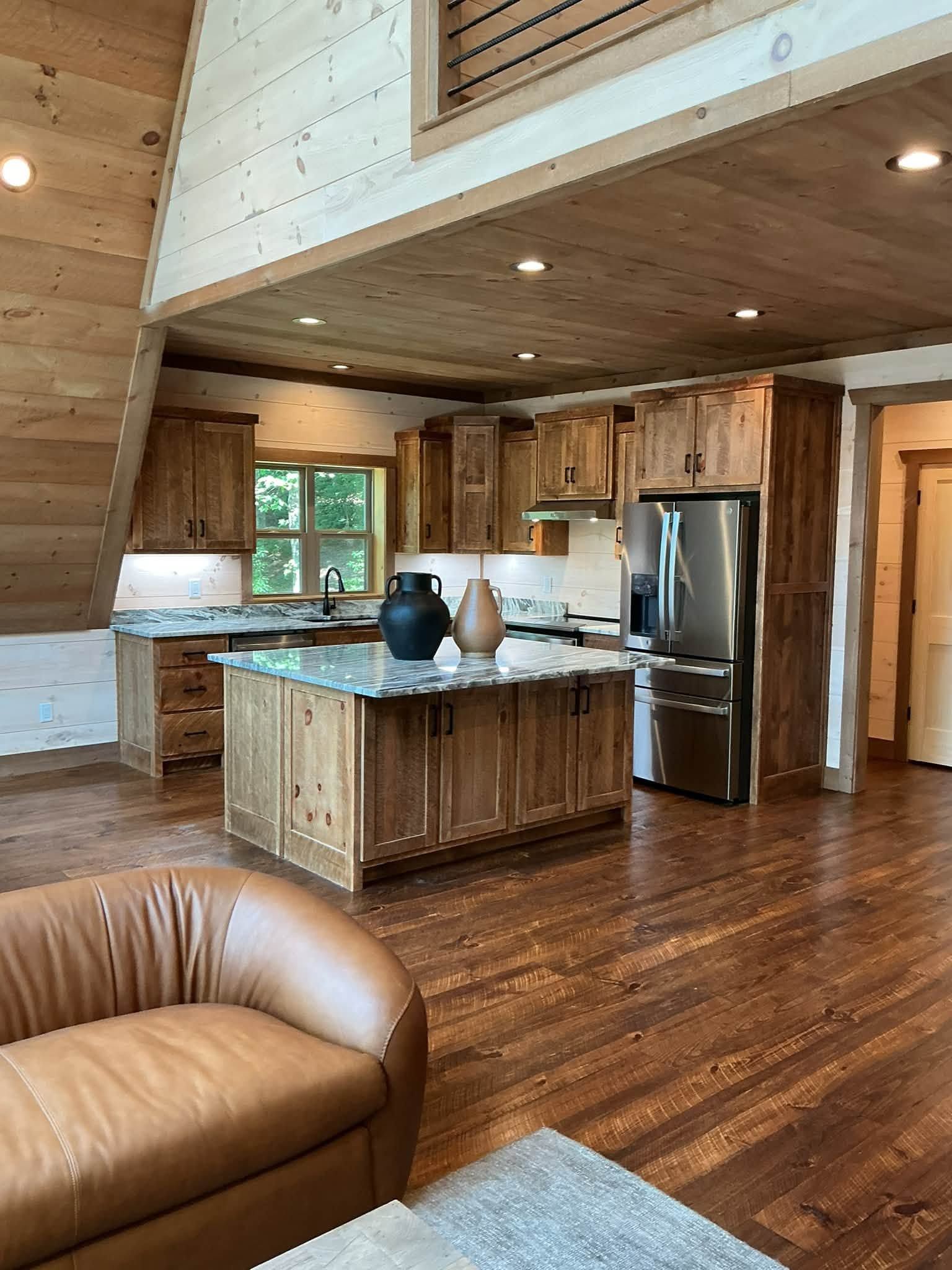 Rustic kitchen with wood cabinets, island, stainless fridge, and open loft ceiling
