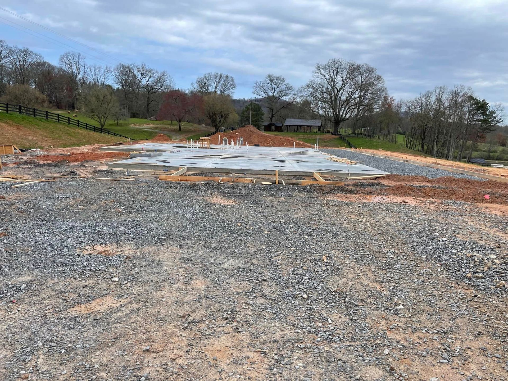 Gravel lot under construction with white pavement sections and trees in the background