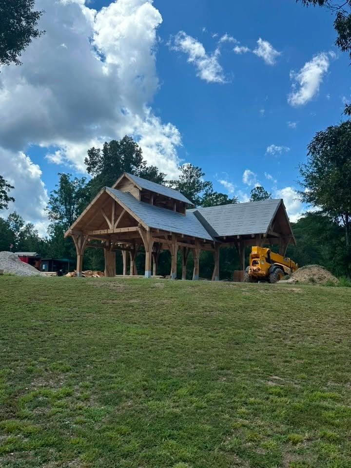 Rustic wooden cabin under construction on a grassy hill, with a yellow excavator and blue sky overhead
