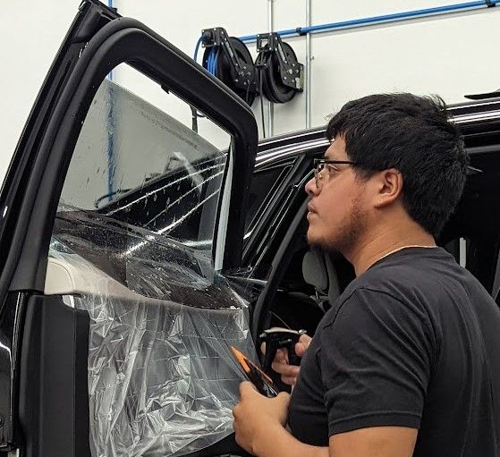 Man applying tint to a car window indoors. He wears glasses and holds a tool.