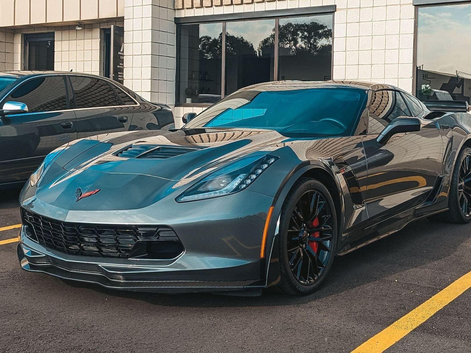 Gray Chevrolet Corvette parked in front of a building with black windows.