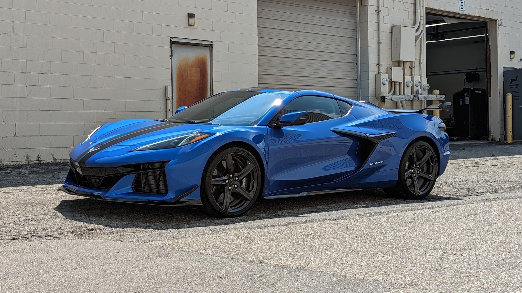 Blue Chevrolet Corvette sports car parked outside a building with a garage door.