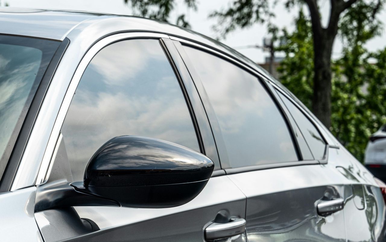 A close up of a car with tinted windows parked next to a tree.