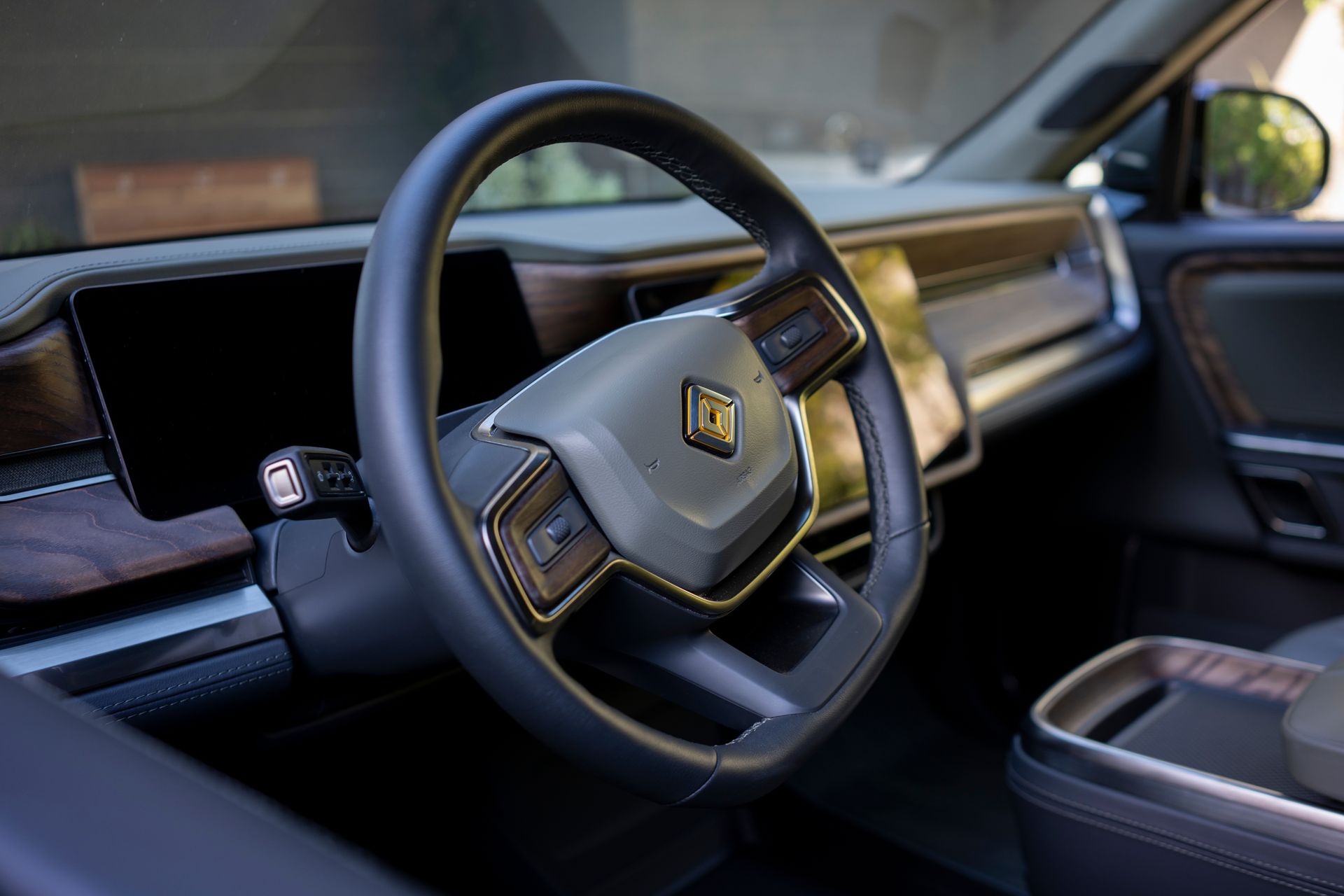 Interior view of a Rivian vehicle with a black steering wheel, dashboard, and wood paneling.