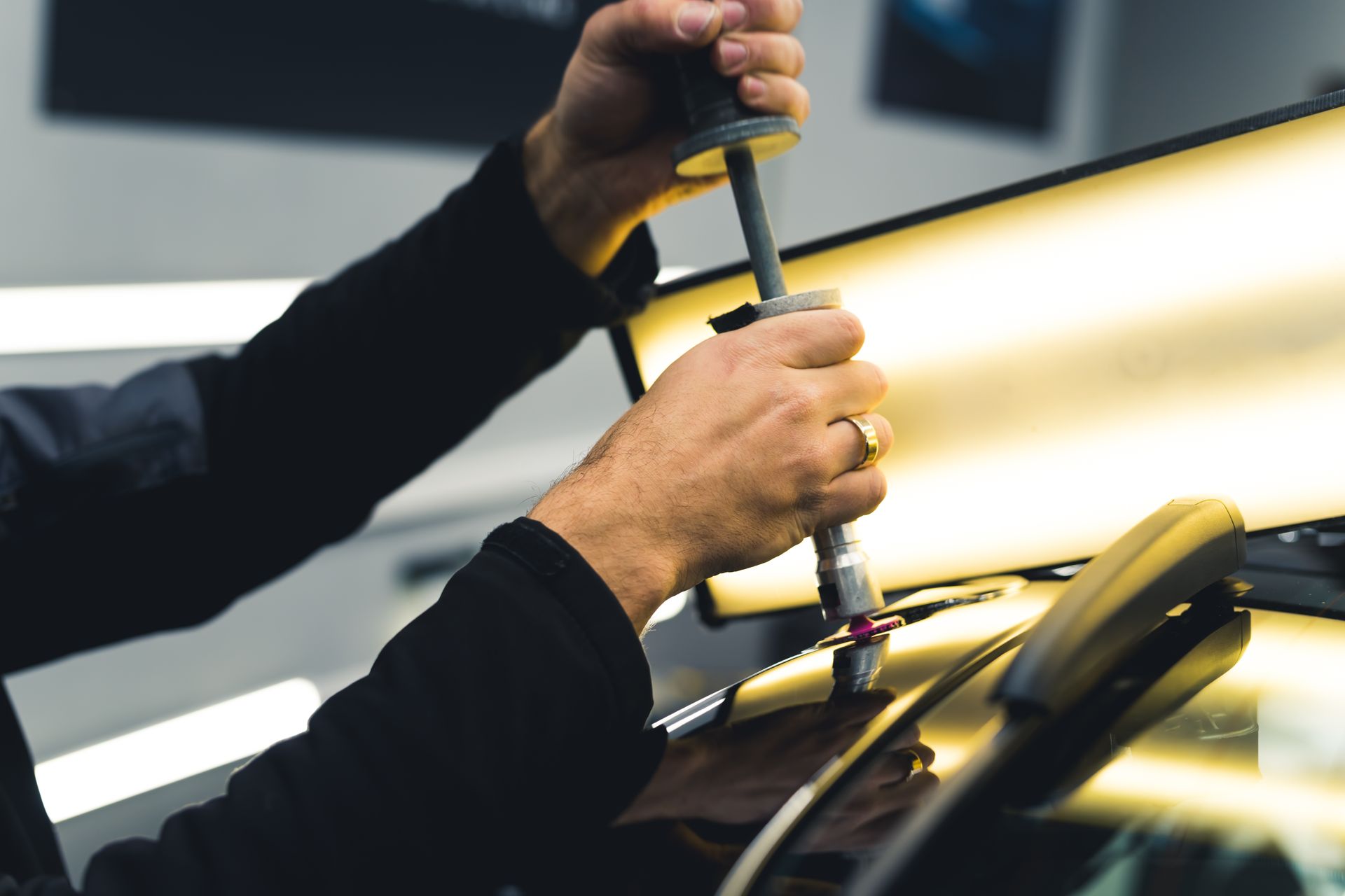 Person using a dent puller tool on a car in a repair shop.