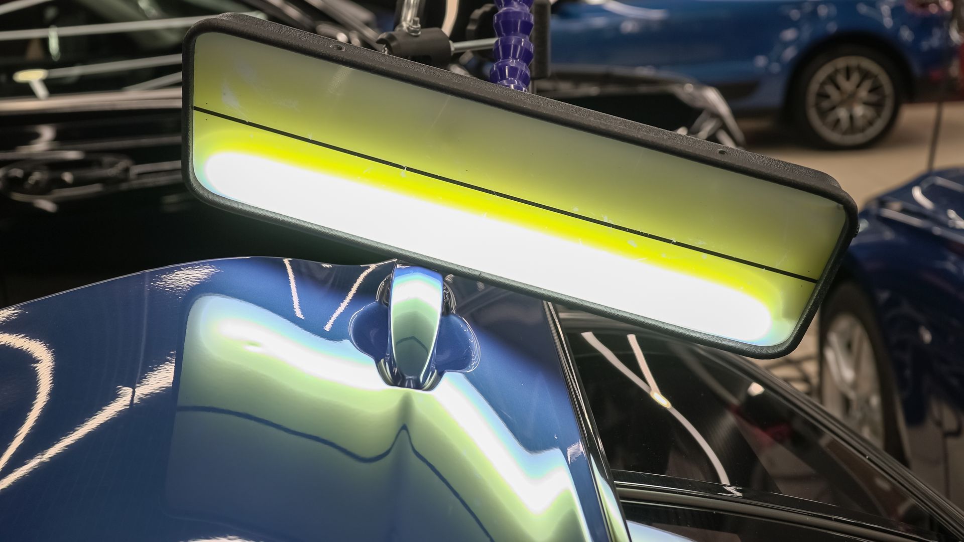 Dent repair on a blue car door. A light reflects on the dent, helping to guide the repair process.