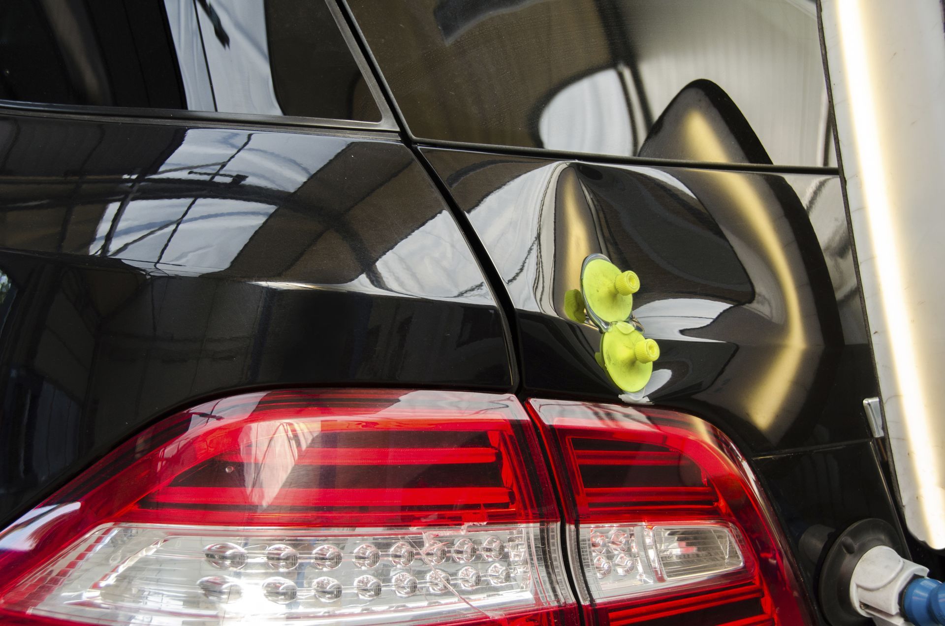 Black car with dent being repaired, yellow suction cups attached, near tail light.