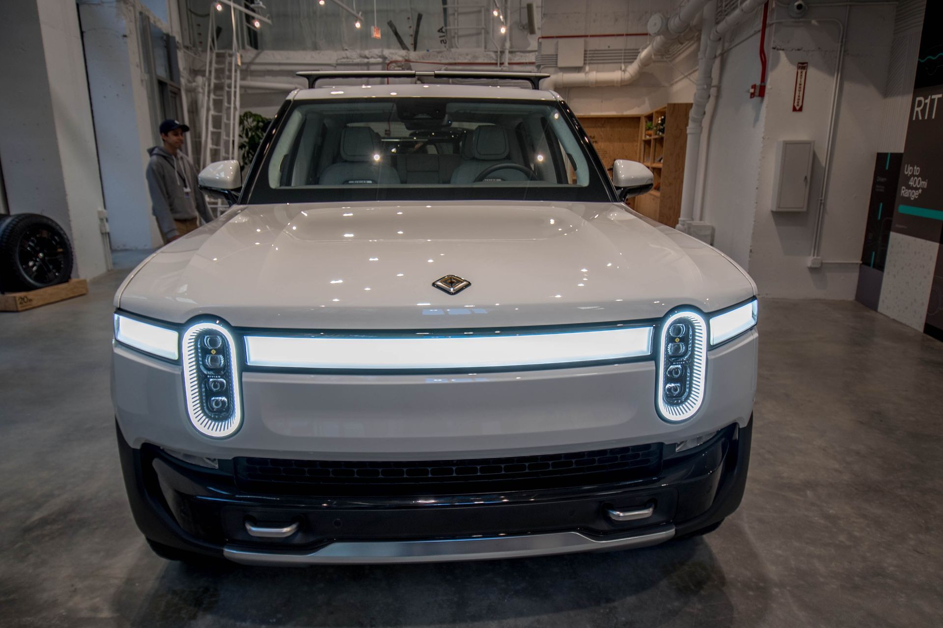 White Rivian SUV with horizontal light bar and vertical headlights, in a showroom.