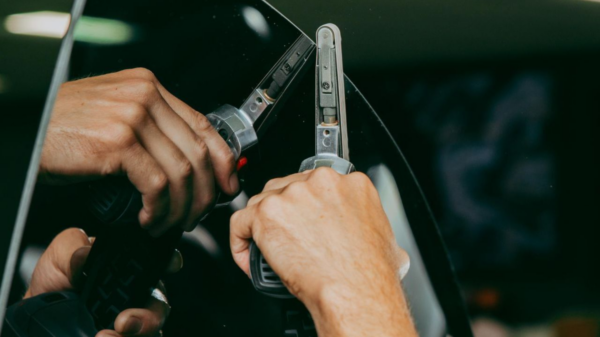 Person tinting a car window, holding tools, reflecting in the dark glass.