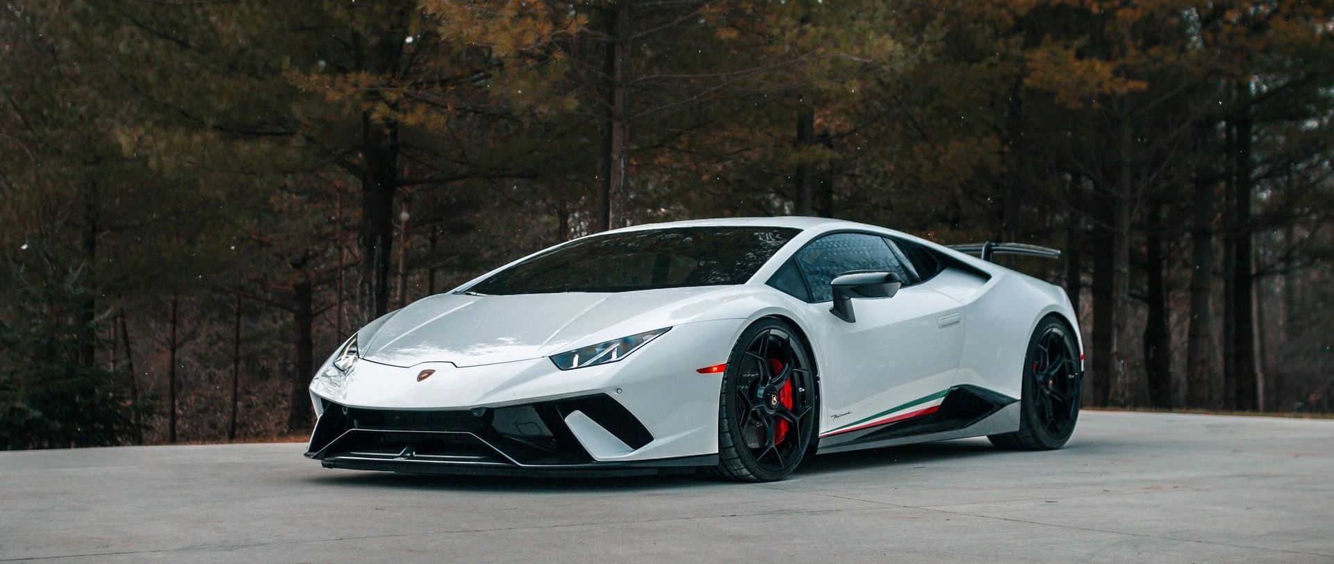 White Lamborghini parked on a road with trees in the background.