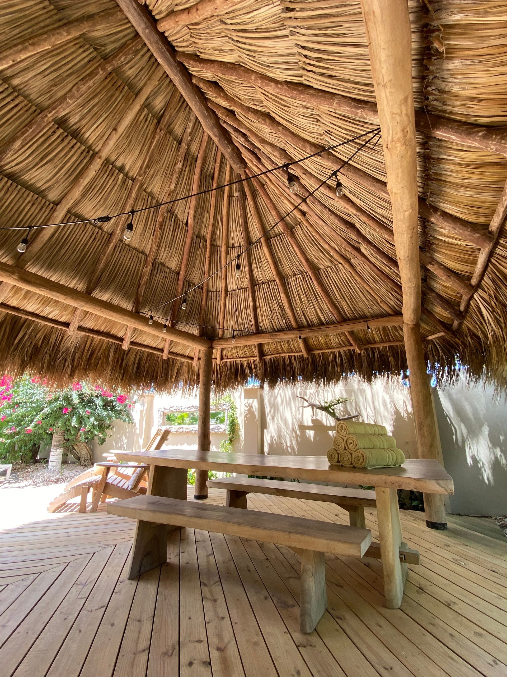 Wooden picnic table under a thatched roof structure on a wooden deck.