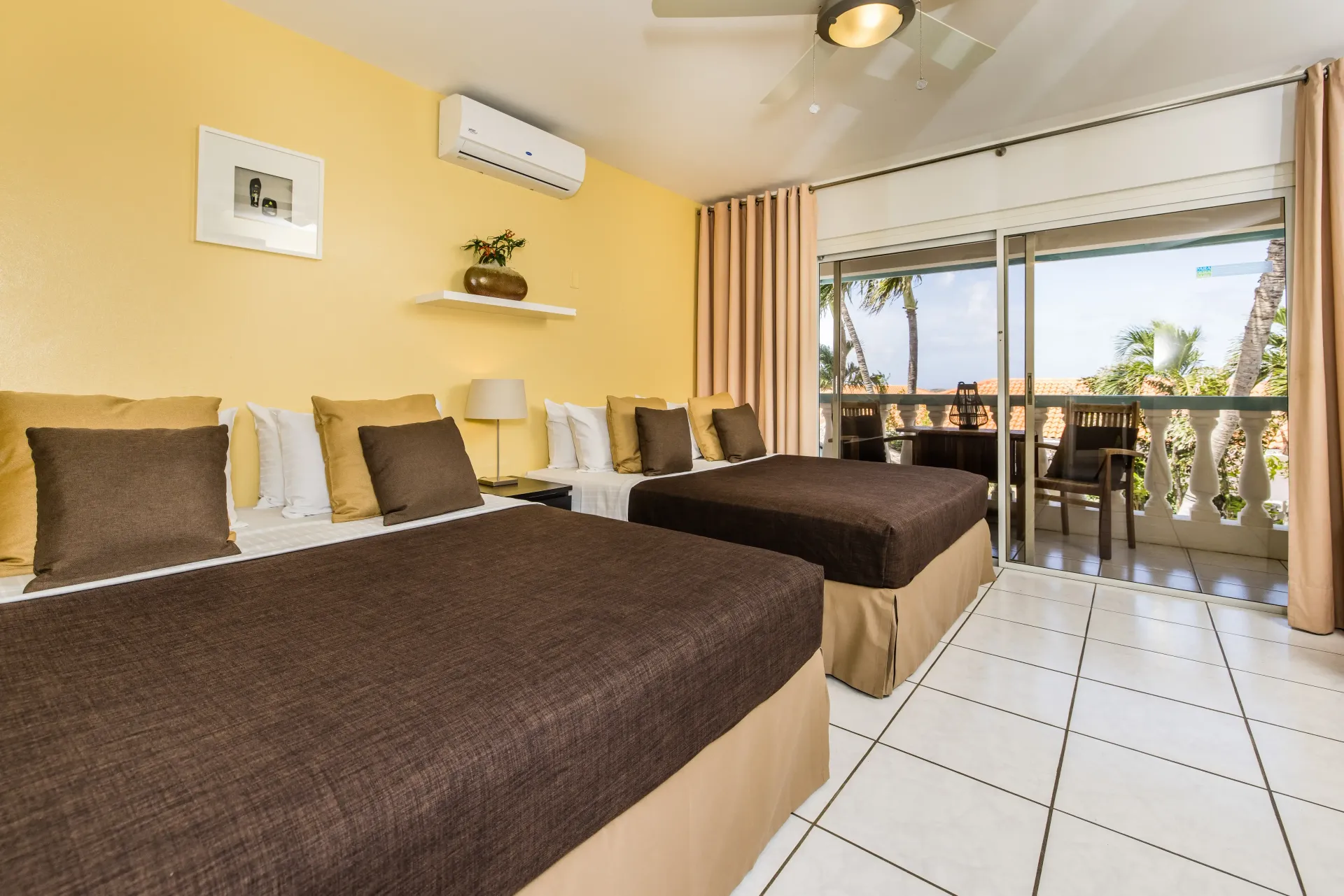 Two brown beds in a yellow-walled room with sliding doors to a balcony.