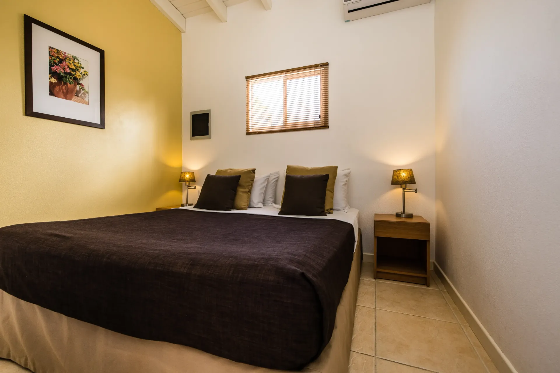 Bedroom with a brown bedspread, nightstand with lamp, and art on the wall.