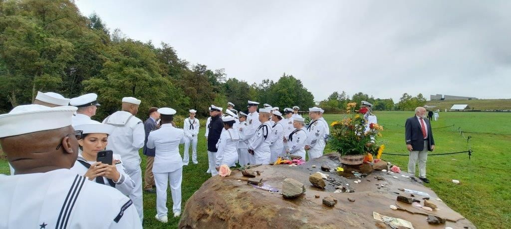 A group of people in white uniforms are standing around a large rock.