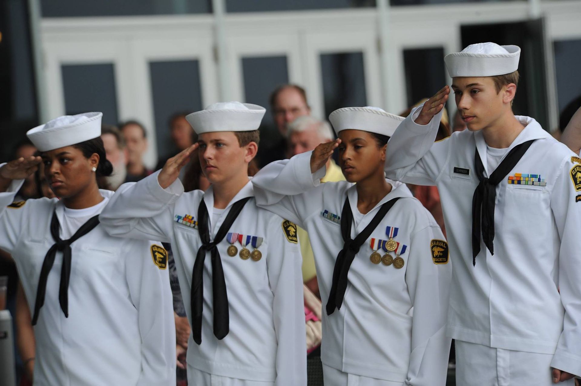 A group of sailors salute in front of a crowd