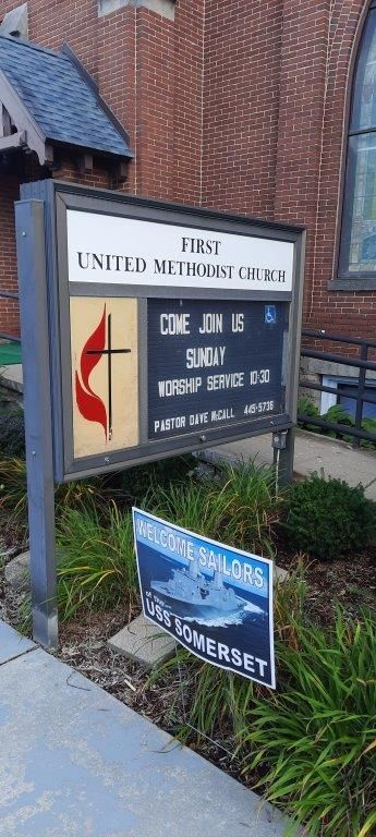 A sign for the first united methodist church is sitting in front of a brick building.