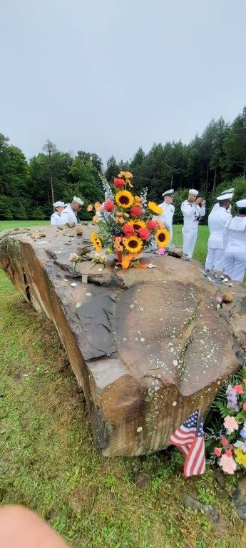 A group of people are standing around a large rock with flowers on it.