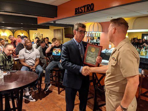 A man in a suit is shaking hands with a man in a military uniform in a restaurant.