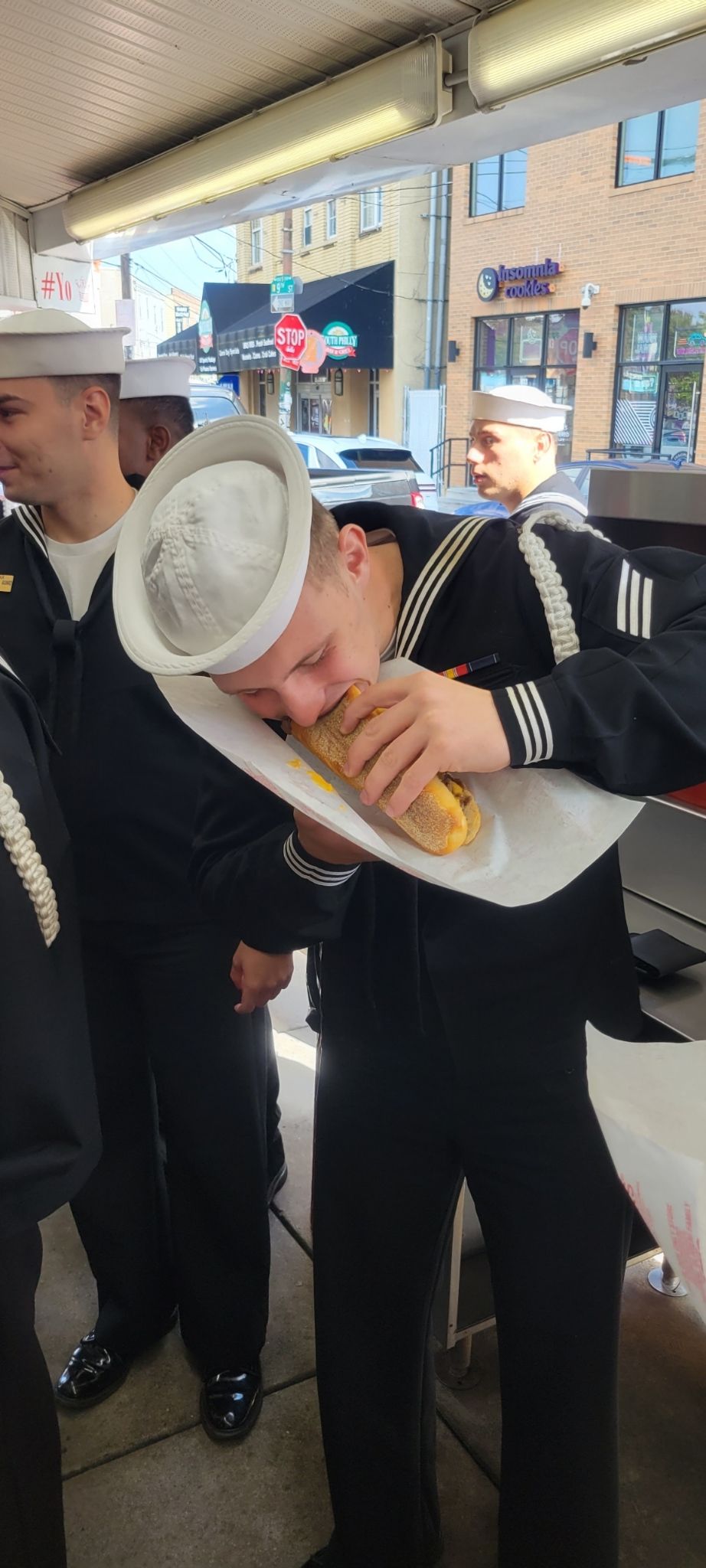 A man in a sailor hat is eating a hot dog