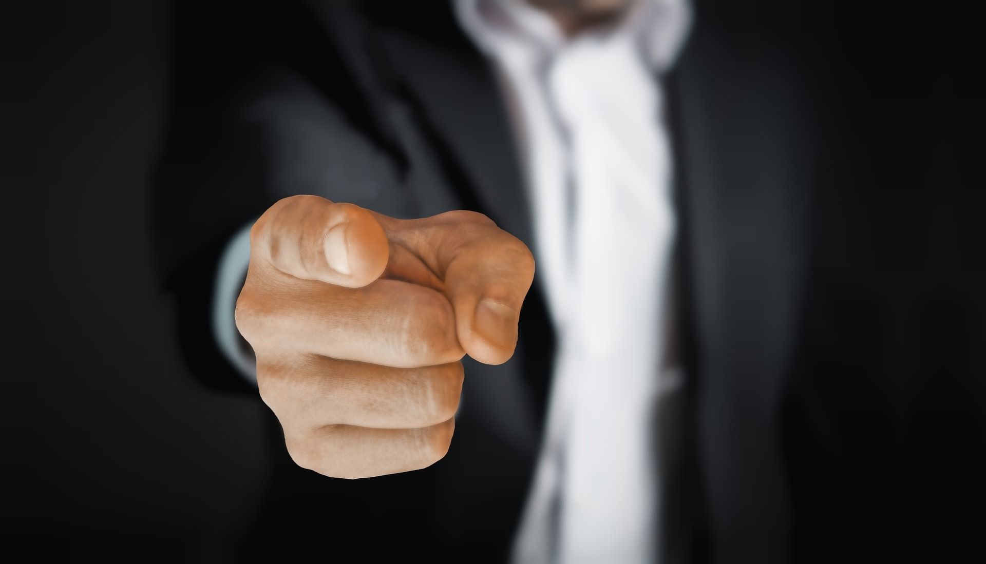 A man in a suit and tie is pointing his finger at the camera
