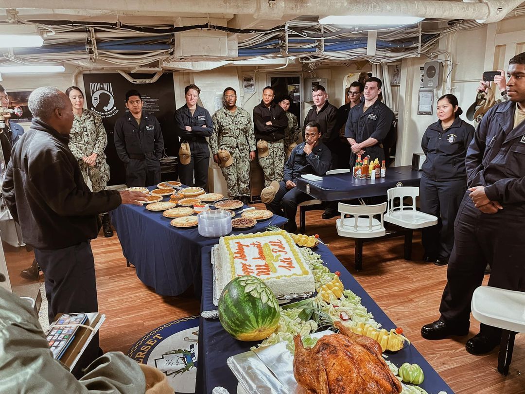 A group of people are standing around a table with food on it.