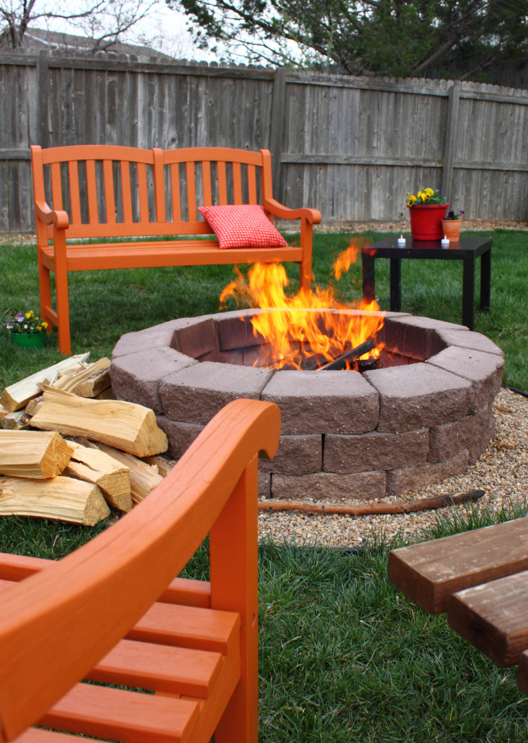 Fire pit in a backyard with colorful benches on the grass
