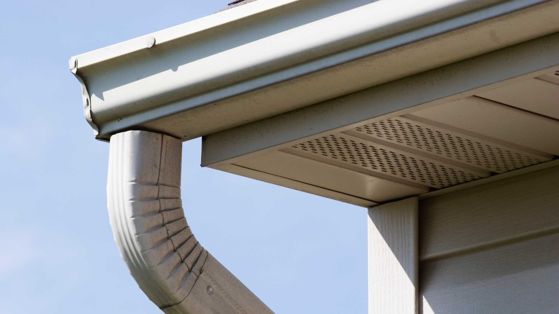 Close-up of a house gutter and downspout under a roof, against a blue sky