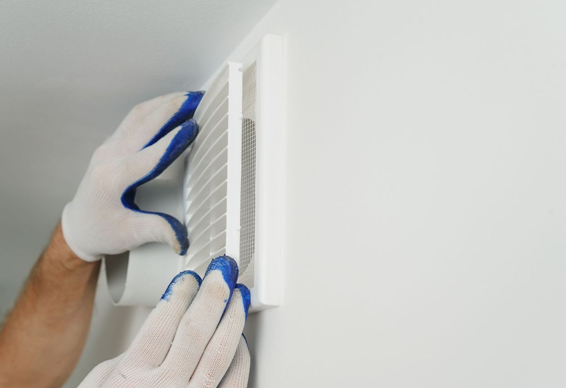 Hands in gloves attaching a white air vent cover to a white wall.