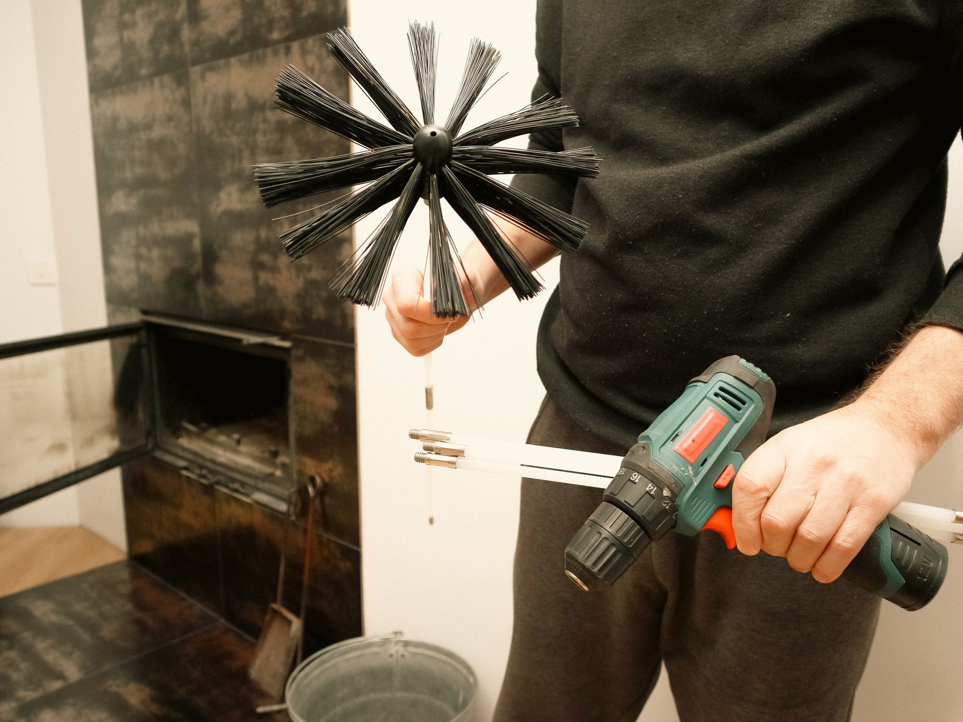 Person cleaning a fireplace chimney with a brush attached to a drill. Person cleaning a fireplace chimney with a brush attached to a drill.